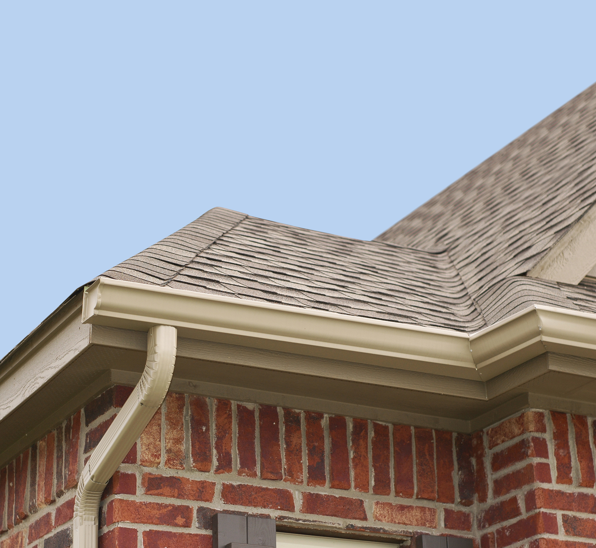 The corner of a red brick house with beige gutters.